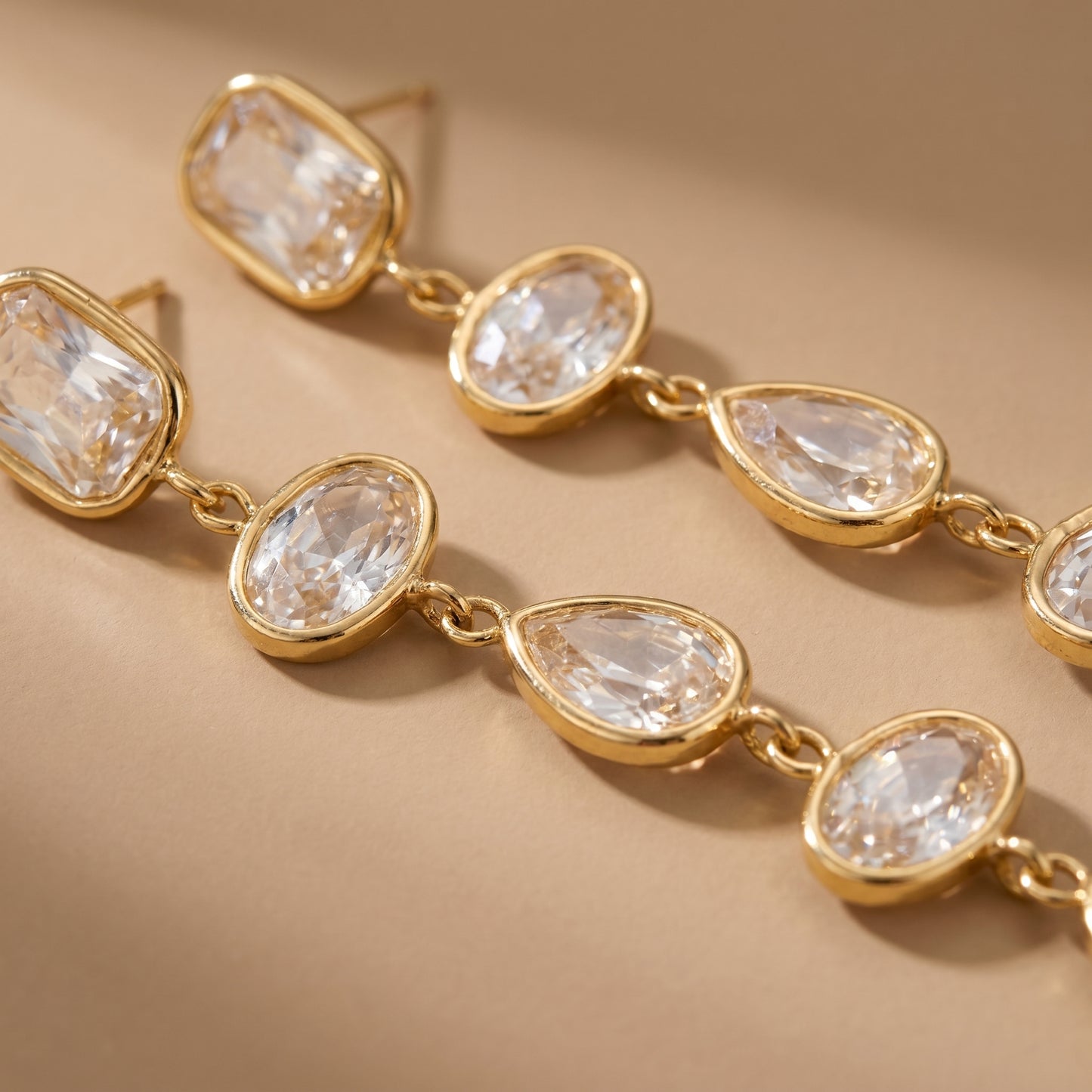 Gold earrings with clear gemstones on a beige background