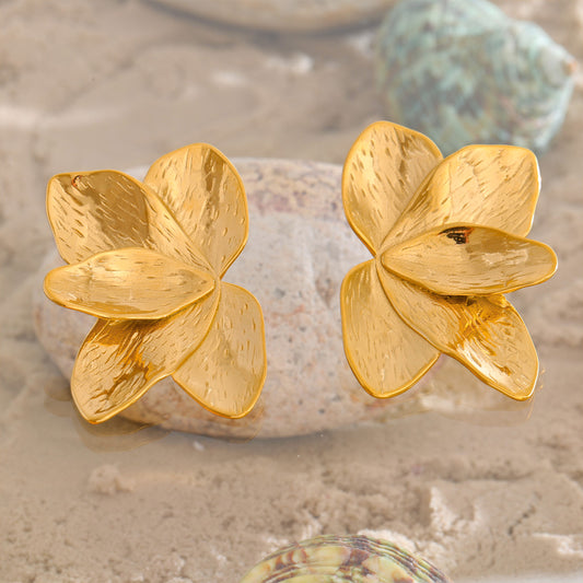 Gold flower-shaped earrings on a textured surface. latest earring models and trending earrings models. new arrivals.