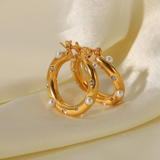 Gold hoop earrings with pearl and gemstone accents on a beige fabric background