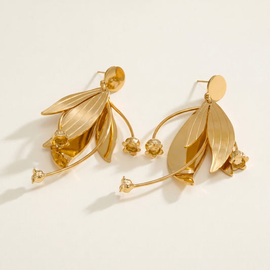 Gold leaf-shaped earrings on a light beige background