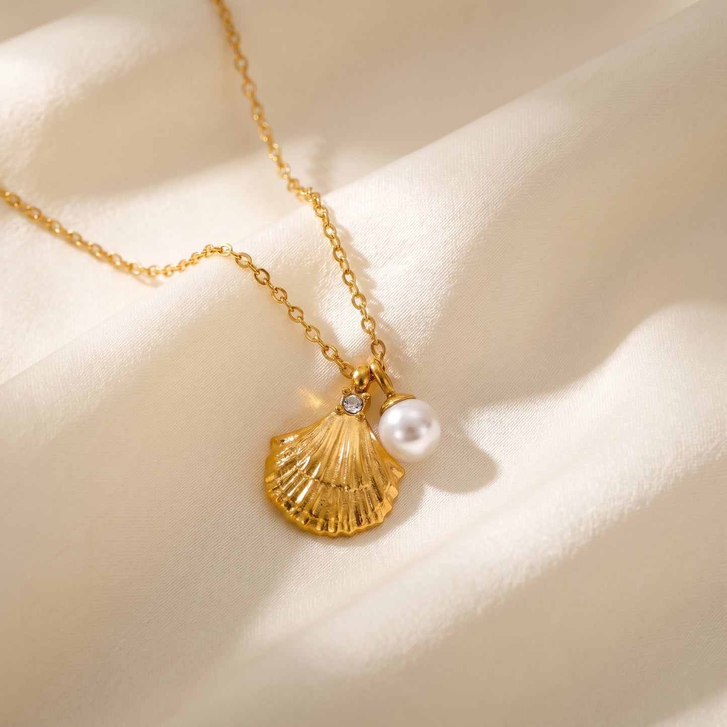 Gold necklace with shell and pearl pendant on a beige background