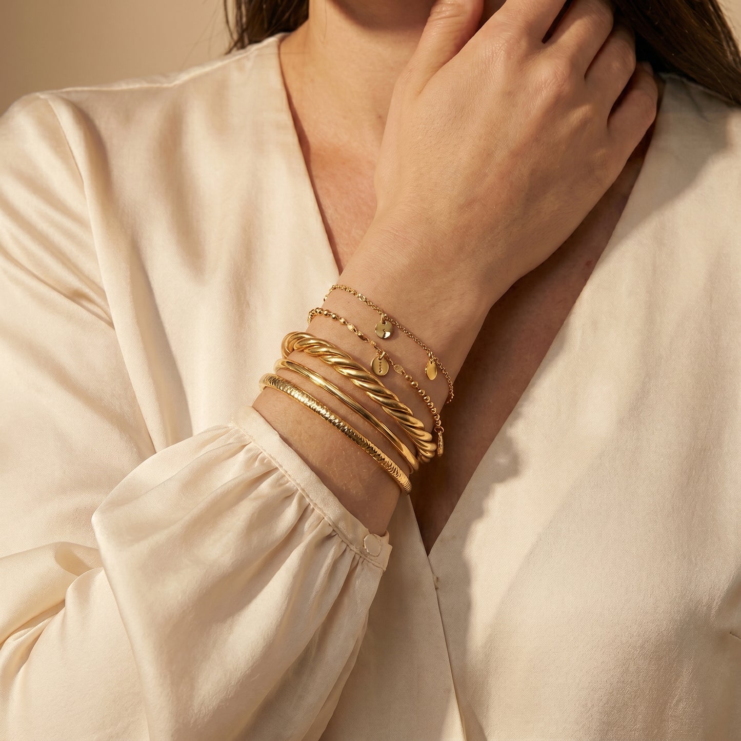 Close-up of a person wearing high quality Sienne Twisted Cuff Bangle by Floravisha on a beige background.