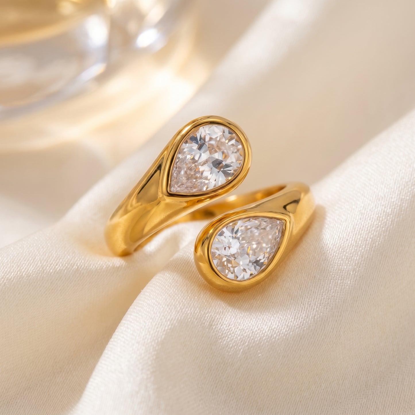 Soleil Toi et Moi Adjustable Ring by Floravisha. A high quality, waterproof gold plated open wrap ring featuring two brilliant teardrop-cut clear crystals. Elegant, tarnish-free, and skin friendly on a soft beige fabric background.