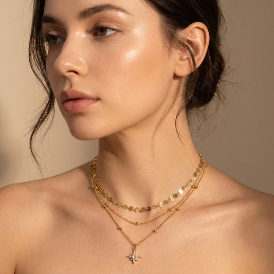 Triple chain layered gold starburst necklace on a model's collarbone in warm natural sunlight.
