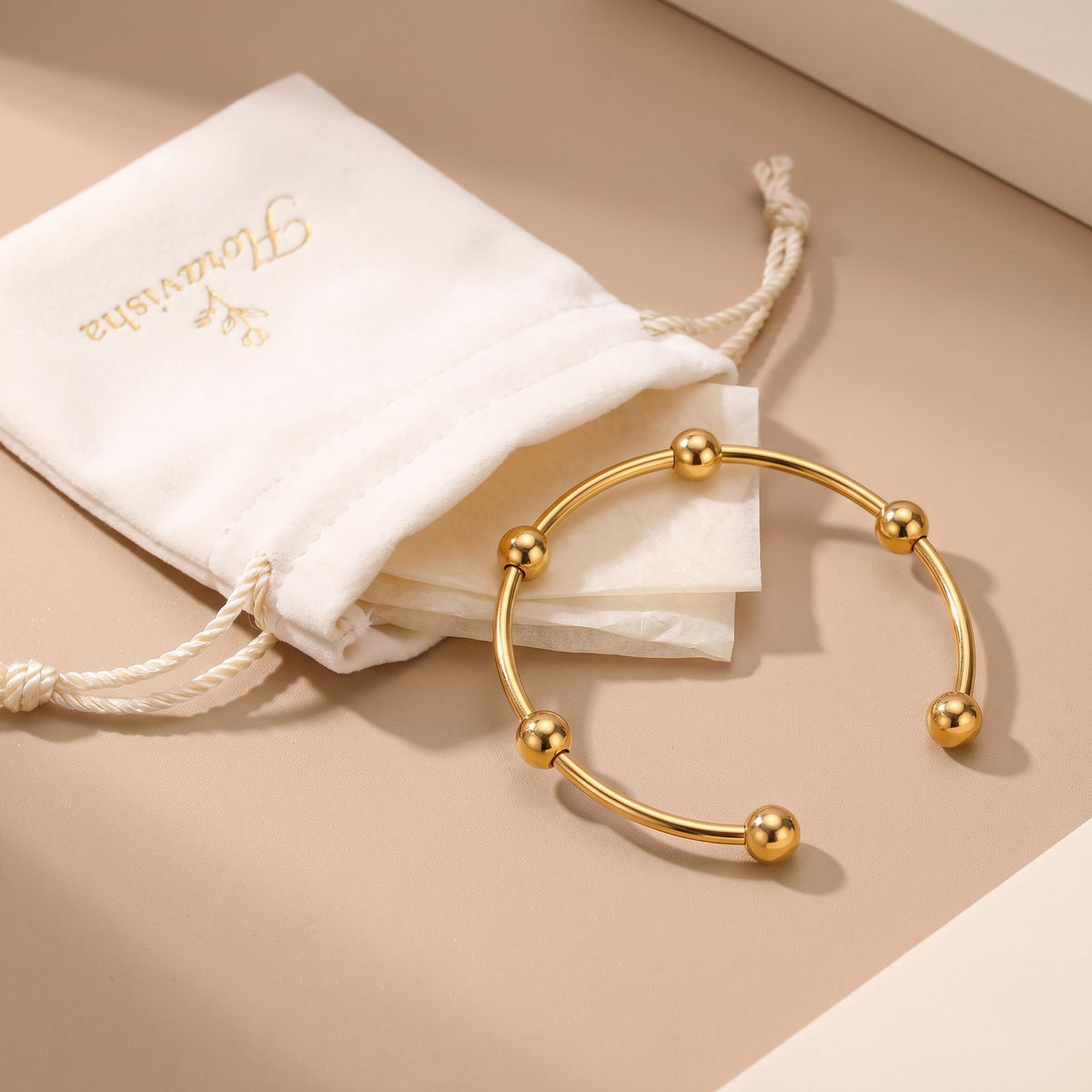 Waterproof Astrid gold beaded open cuff bangle resting next to an off-white Floravisha luxury drawstring velvet pouch.