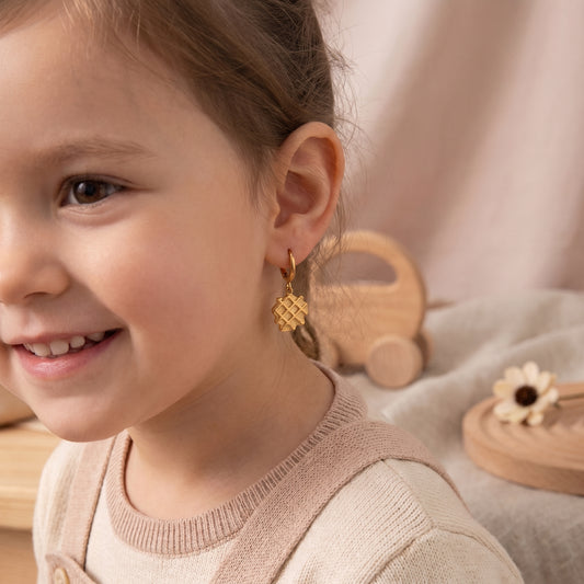Close-up of a smiling young girl wearing the lightweight, hypoallergenic La Gaufre gold waffle charm huggie earrings with a beige knit top.