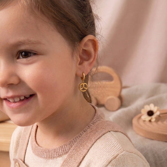 Close-up of a smiling young girl wearing the lightweight, hypoallergenic Le Bretzel gold pretzel dangle huggie earrings with a neutral knit sweater.