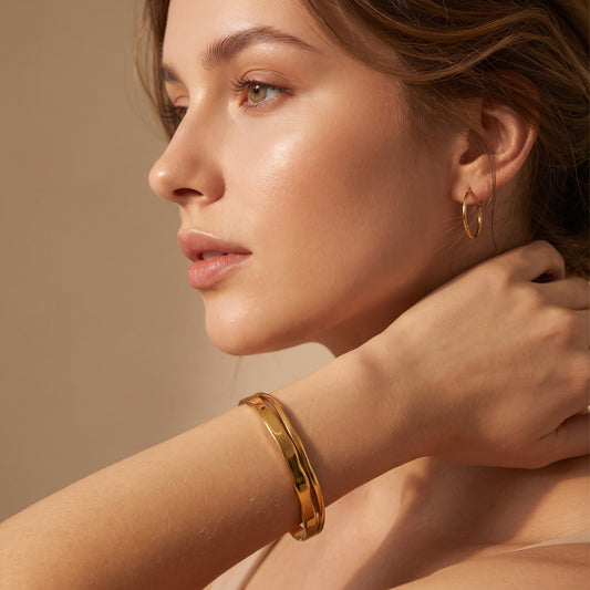 High quality Ondine gold double-layered organic wave cuff bangle worn on a model's wrist in warm studio lighting.
