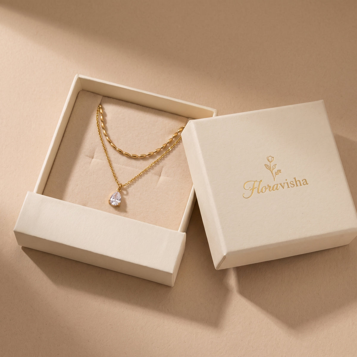 High quality Seraphine gold layered teardrop necklace presented inside an open off-white Floravisha luxury sliding jewelry gift box.