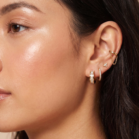 Modern gold ear stack on a woman featuring the skin friendly Verona baguette crystal huggie paired with a pavé hoop and chain cuff.