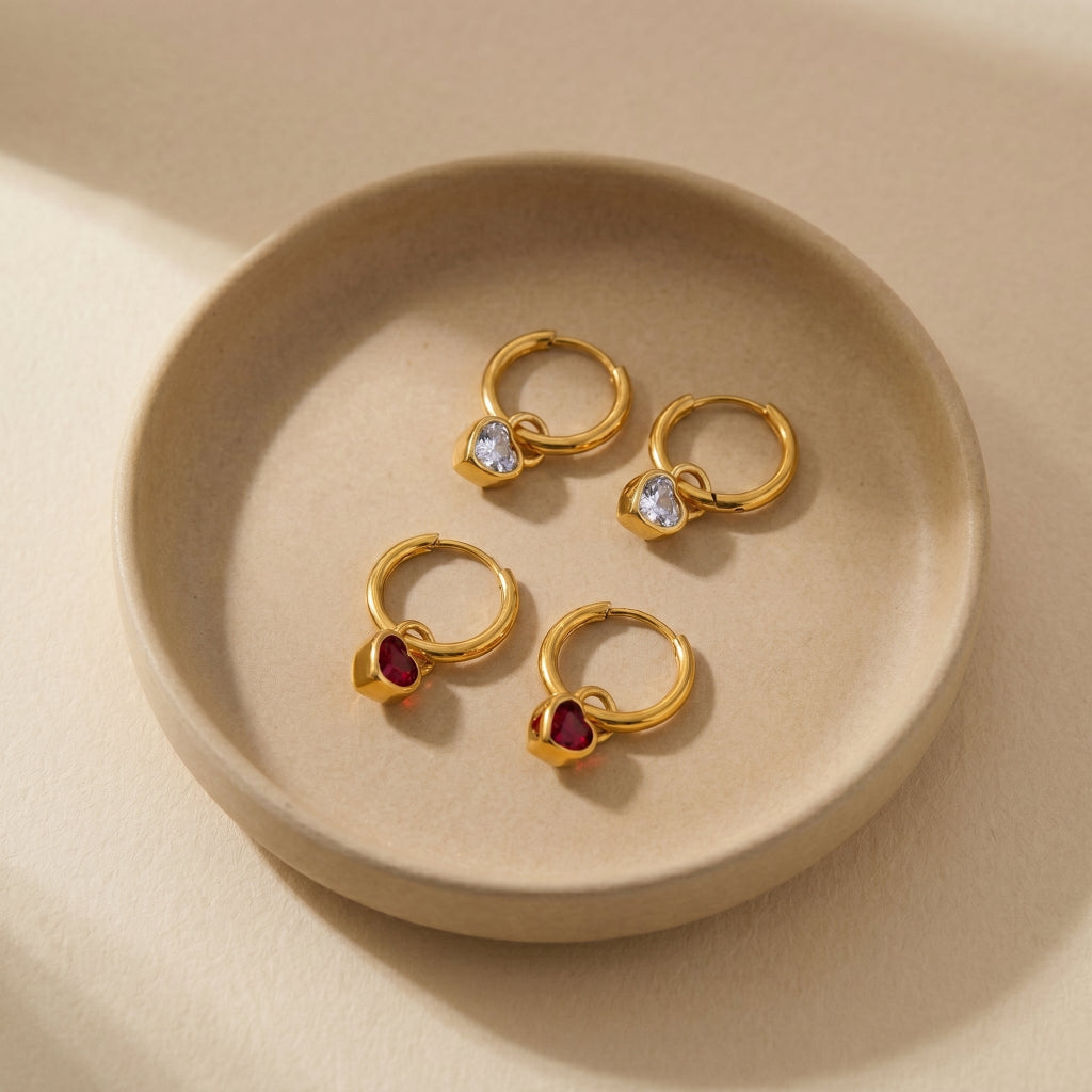 High quality waterproof gold plated huggie hoop earrings featuring sparkling ruby red and clear crystal heart dangle charms, displayed on a clean background