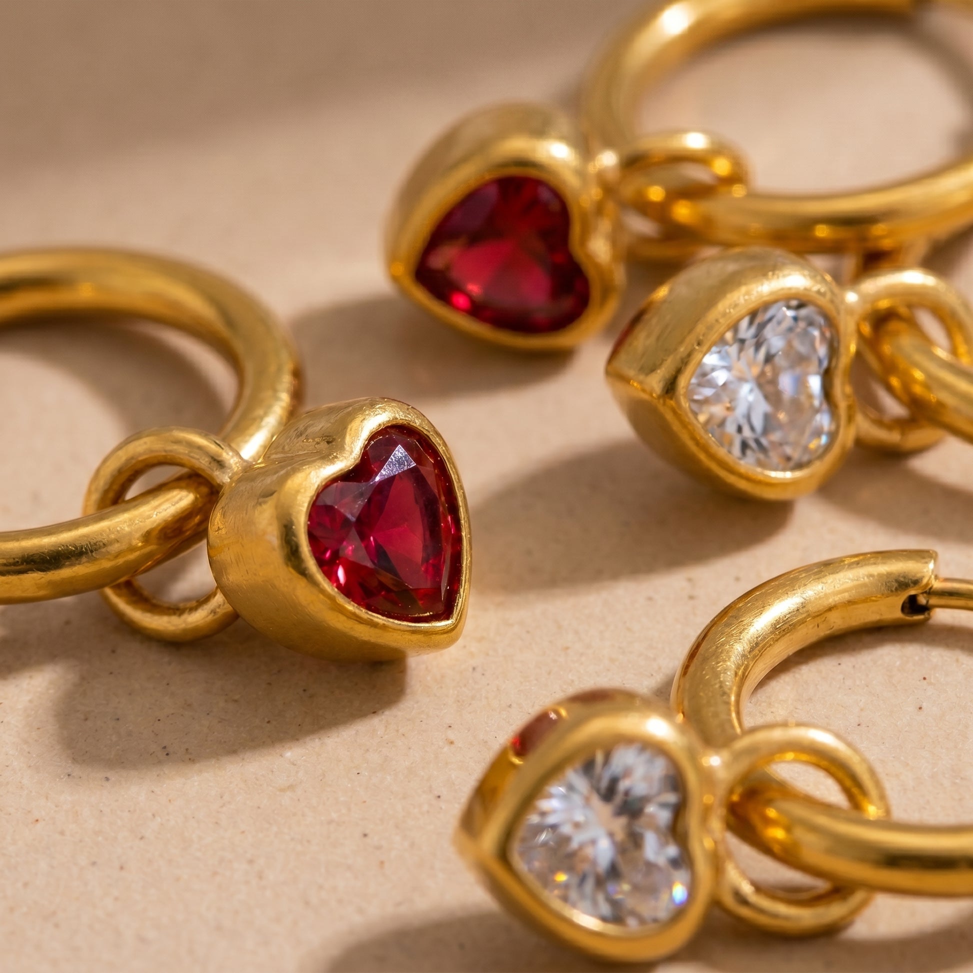 High quality waterproof gold plated huggie hoop earrings featuring sparkling ruby red and clear crystal heart dangle charms, displayed on a clean background