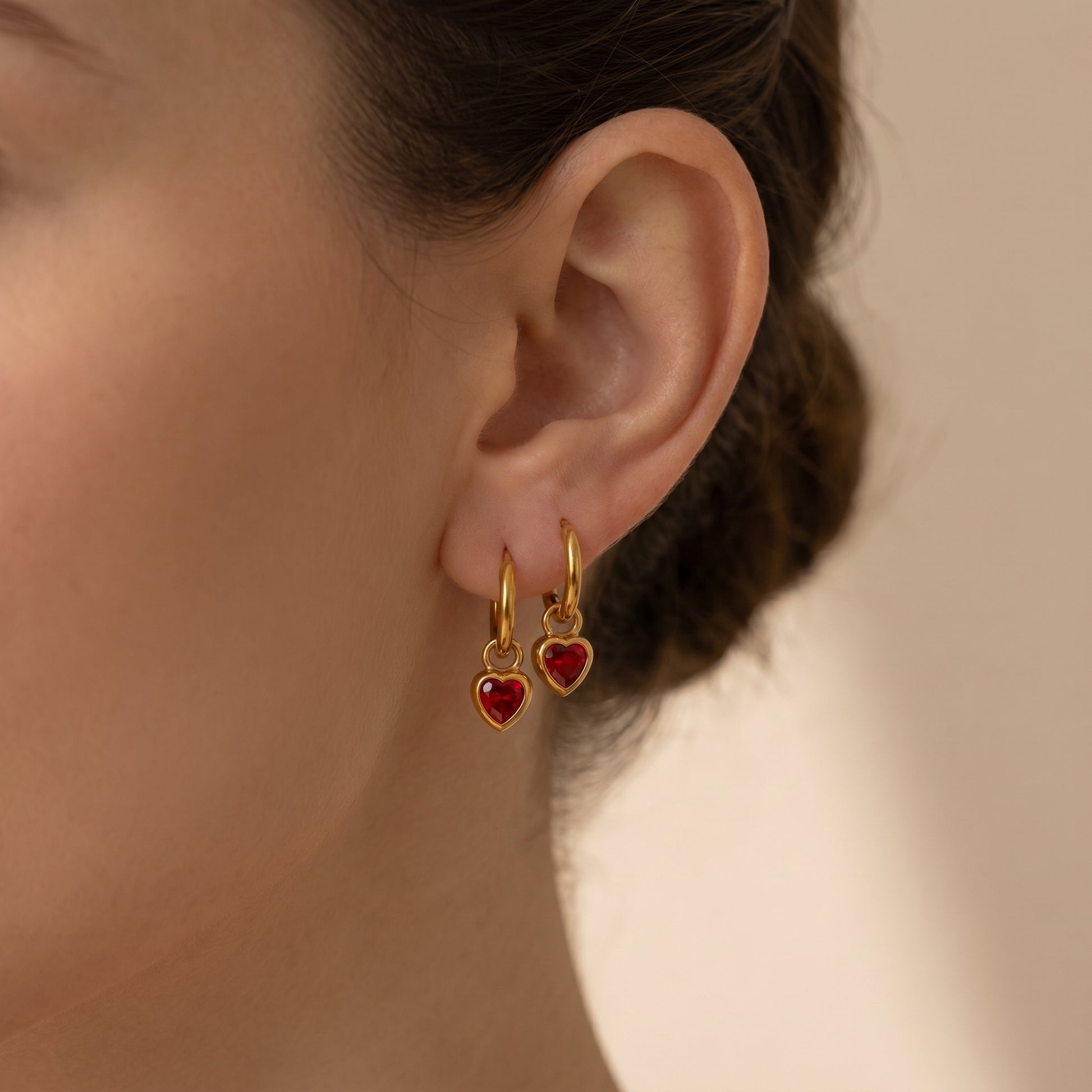 High quality waterproof gold plated huggie hoop earrings featuring sparkling ruby red heart dangle charms, displayed on a clean background