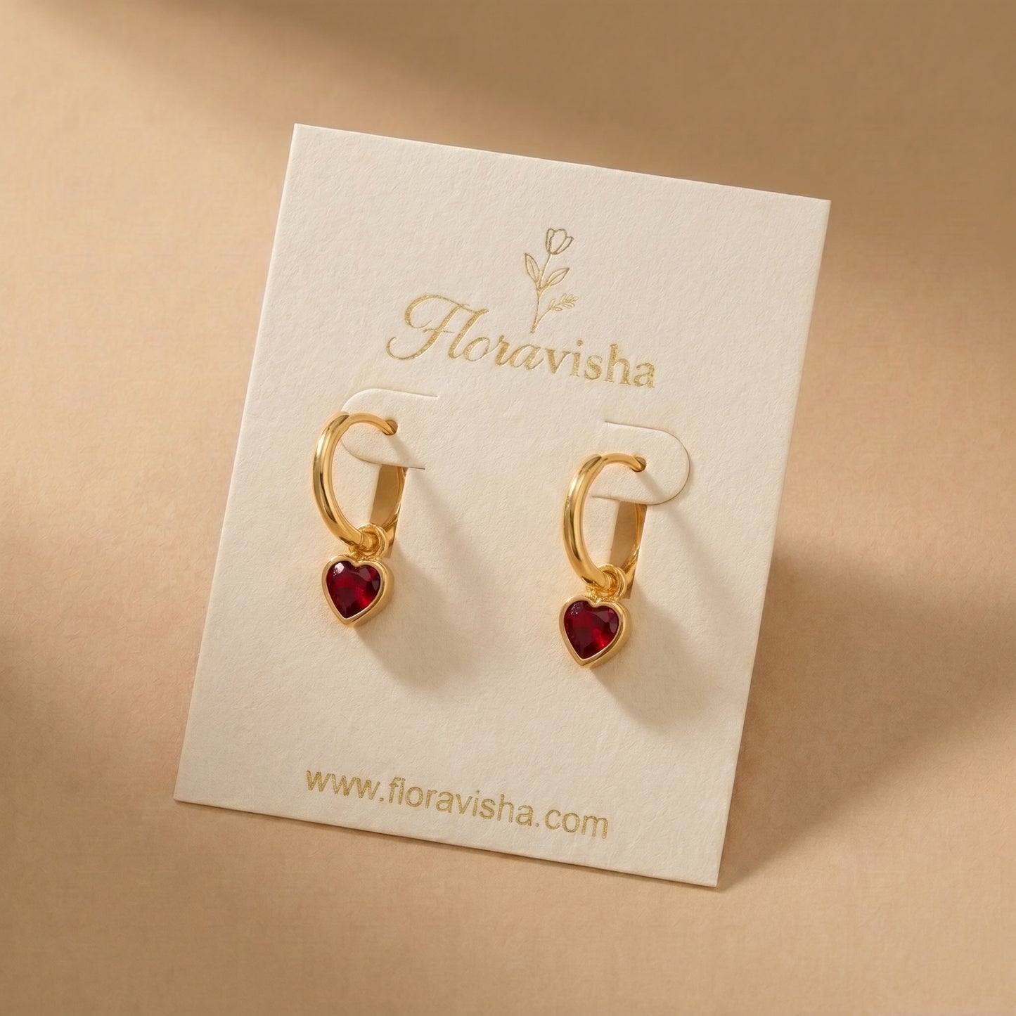 High quality waterproof gold plated huggie hoop earrings featuring sparkling ruby red heart dangle charms, displayed on a Floravisha earrings card.