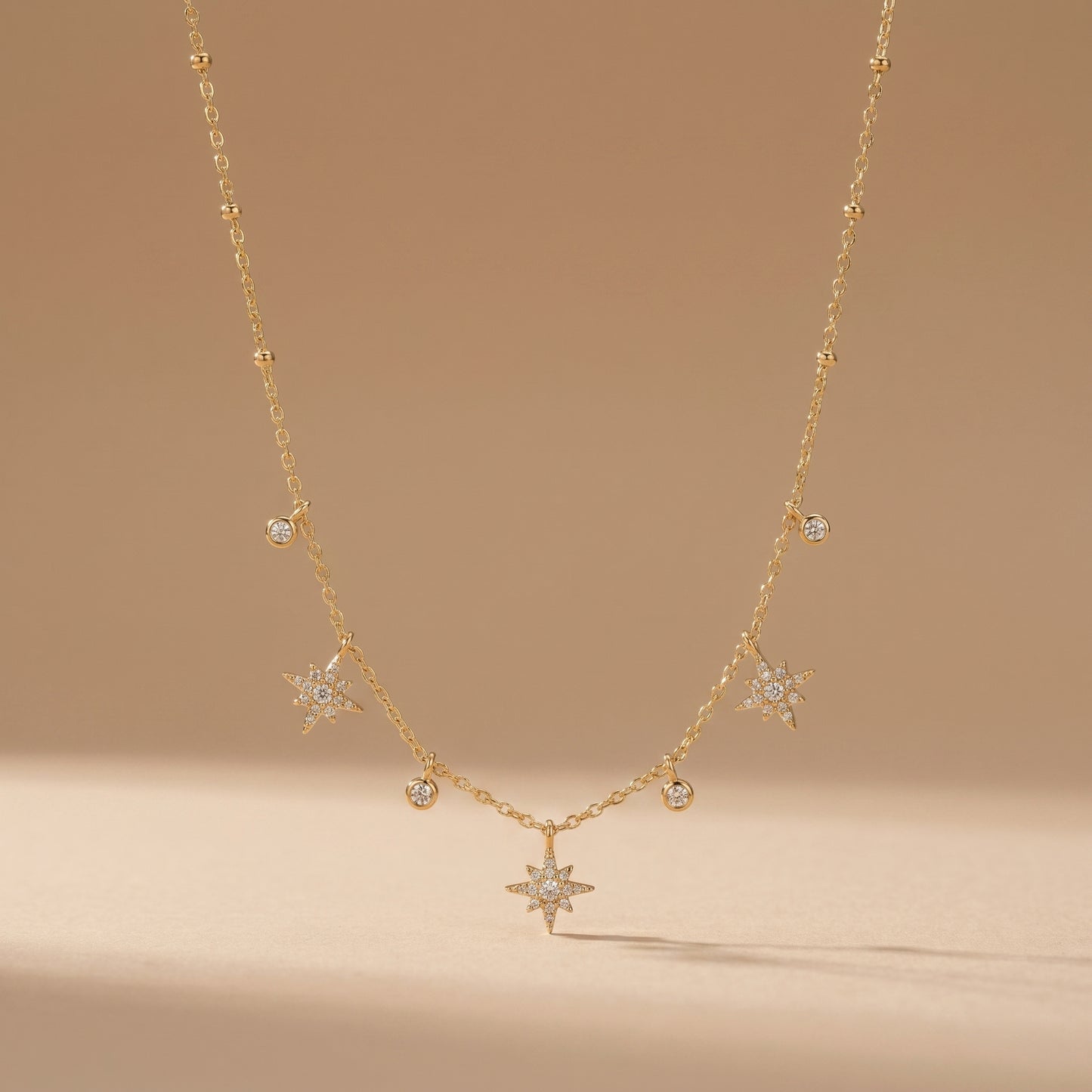 Dainty gold chain necklace featuring alternating dangling starburst charms and clear crystal drops on a clean background, highlighting its tarnish-free and skin friendly finish.