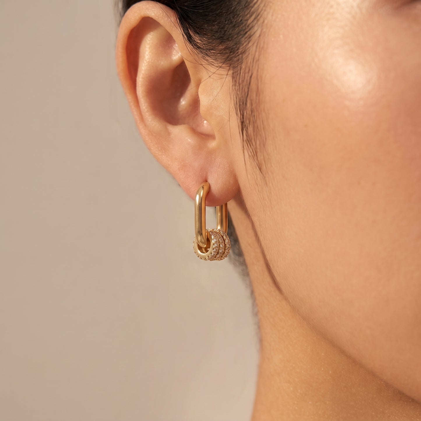 A close-up of a model's ear wearing a The tarnish-free gold Aurelia Eternity Hoops showing a pair of elongated rectangular huggies with three sliding crystal pavé charms