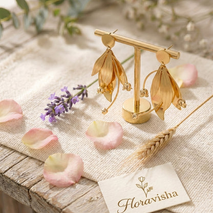 Gold floral earrings on a textured surface with flowers and a 'Floravisha' card.
