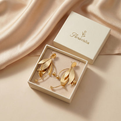 Gold earrings in a box with 'Floravisha' branding on a beige fabric background