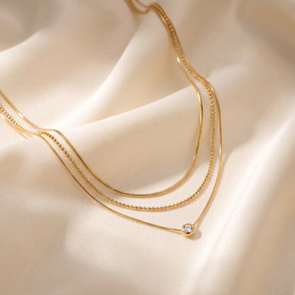 High quality waterproof gold plated triple layer necklace featuring delicate snake chains, a beaded chain, and a solitaire crystal pendant on a white background