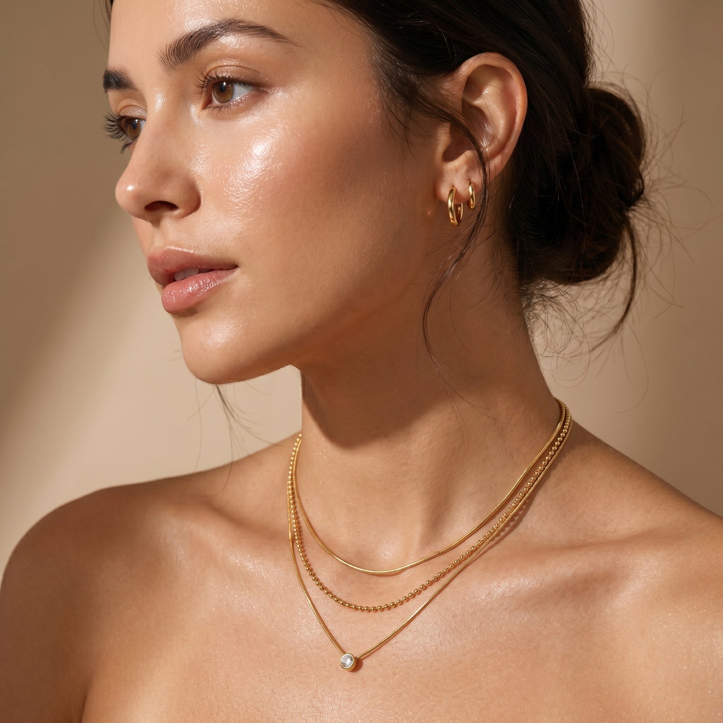 Woman wearing High quality waterproof gold plated triple layer necklace featuring delicate snake chains, a beaded chain, and a solitaire crystal pendant on a beige background.