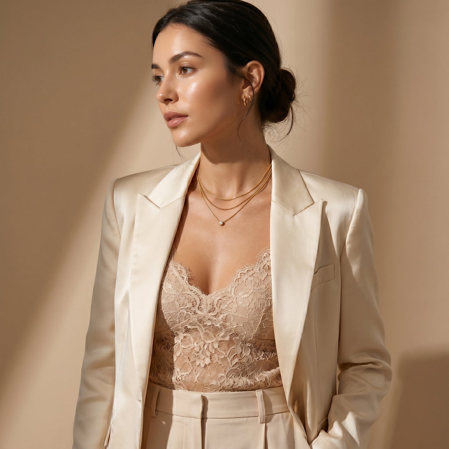Woman wearing High quality waterproof gold plated triple layer necklace featuring delicate snake chains, a beaded chain, and a solitaire crystal pendant and a beige suit with a lace top against a beige background
