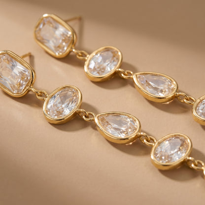 Gold earrings with clear gemstones on a beige background