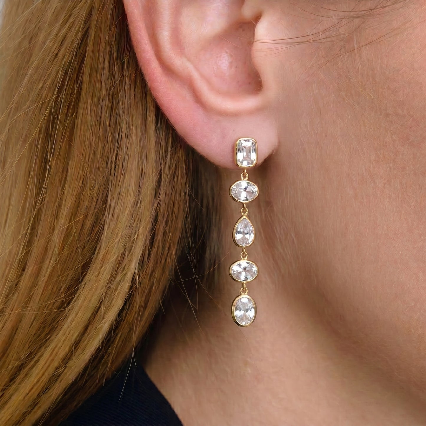Close-up of a person wearing a gold earring with clear stones.