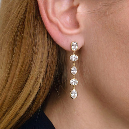 Close-up of a person wearing a gold earring with clear stones.