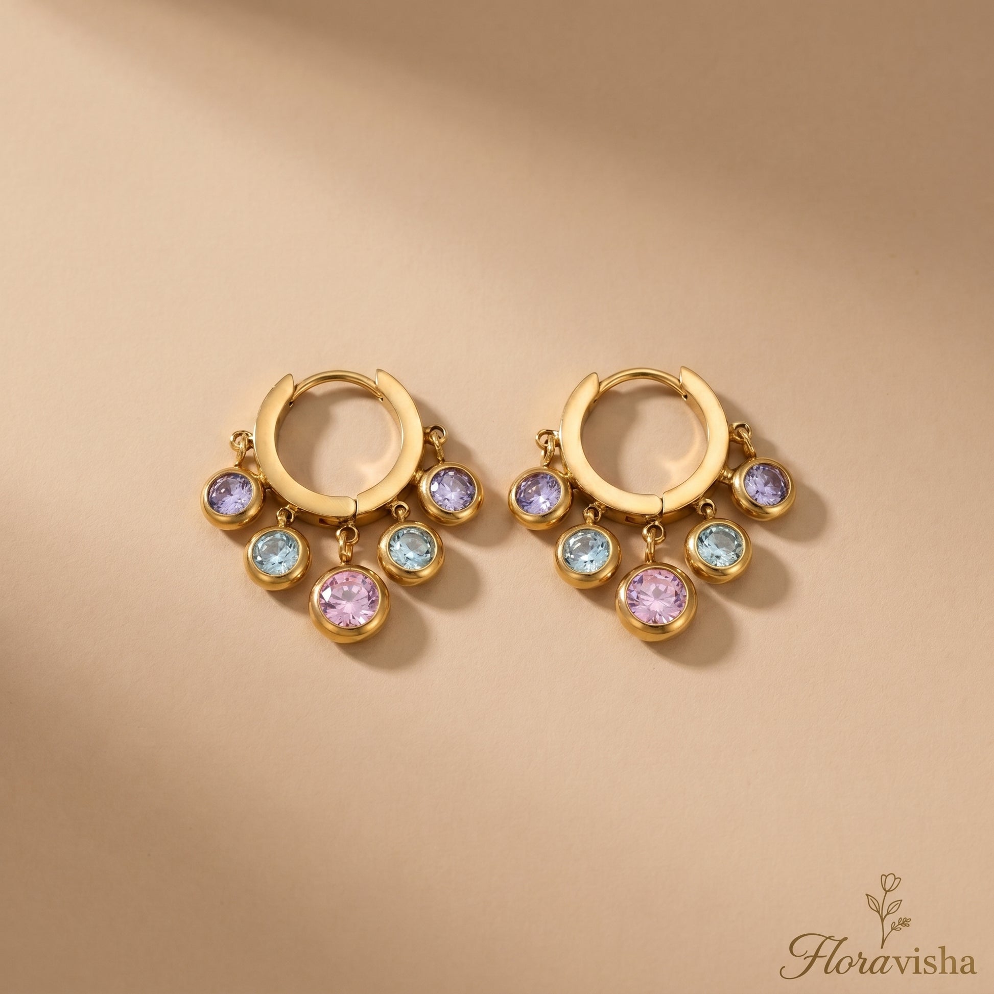 Floravisha multi-color crystal dangle hoop earrings in real gold plating on a tan background.
