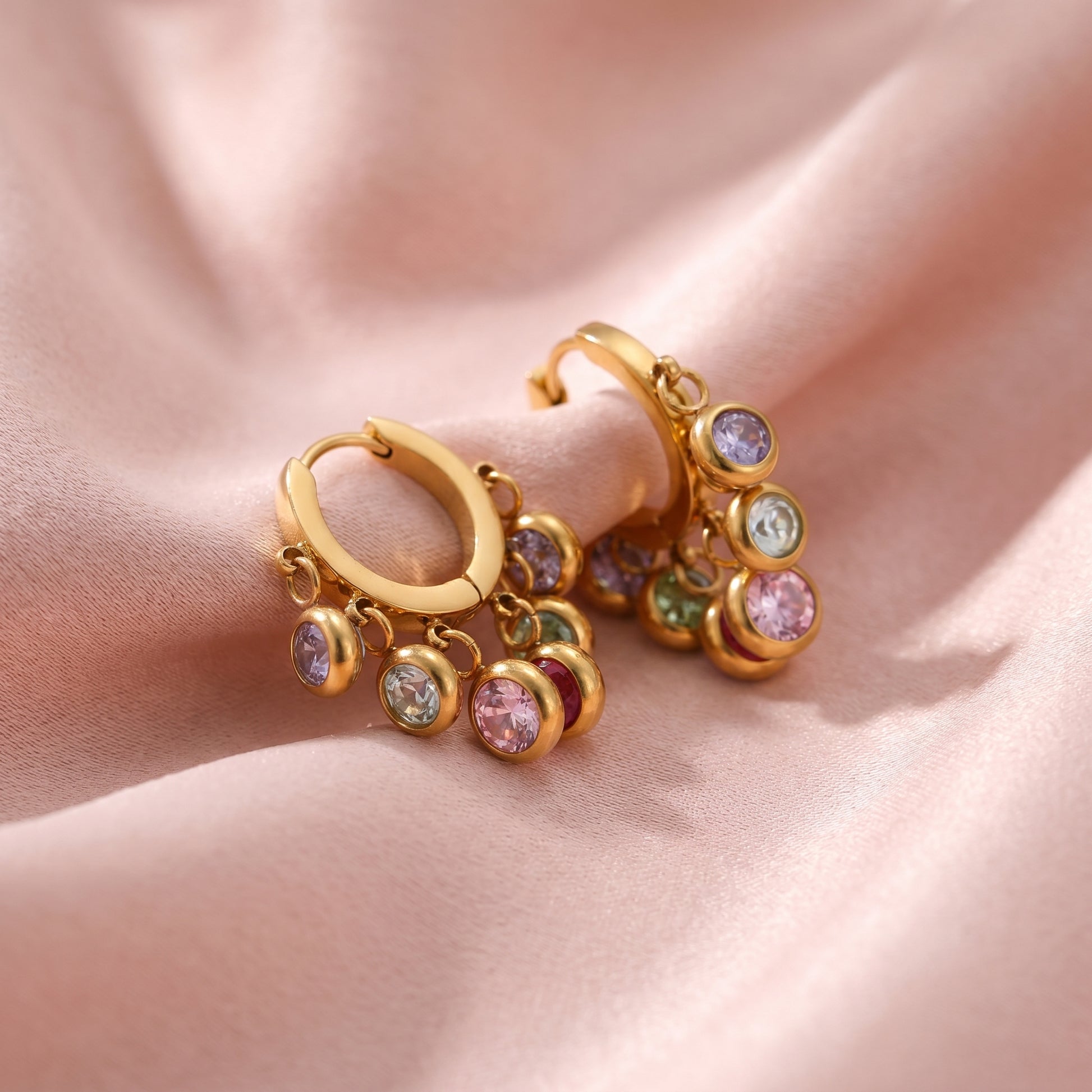 High-angle shot of Gold multi-color crystal earrings on ruffled pink satin material.