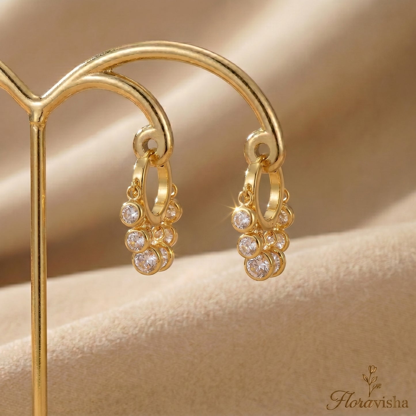 Elegant gold huggie hoops with five clear crystal charms hanging on a gold display.