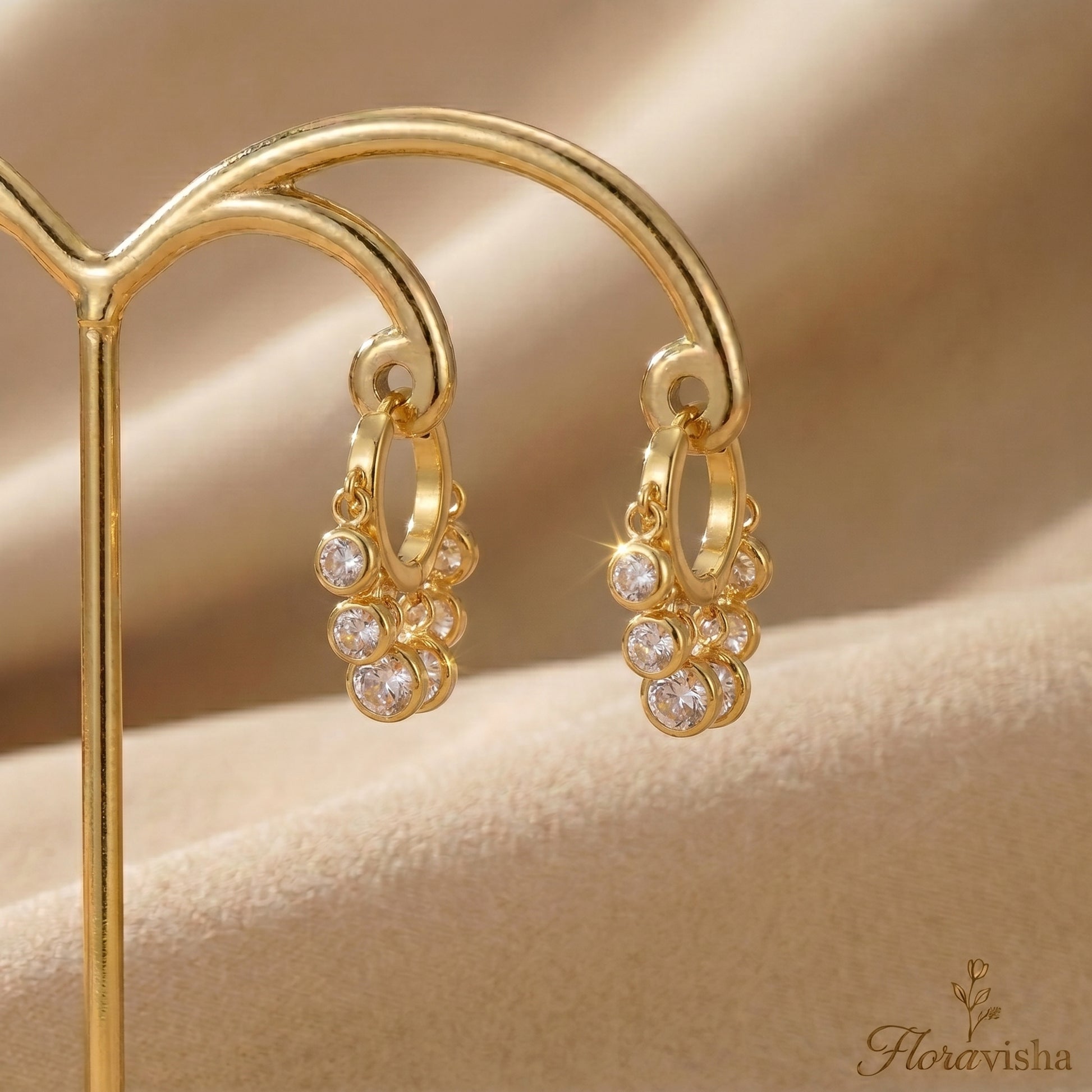 Elegant gold huggie hoops with five clear crystal charms hanging on a gold display.