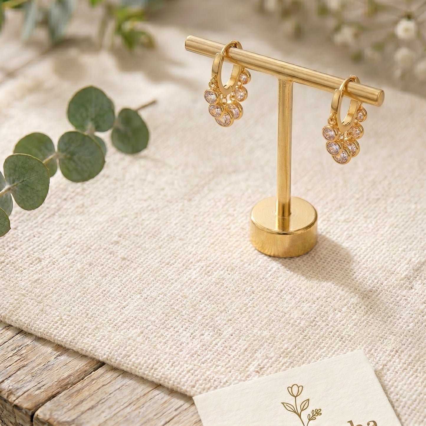 Minimalist gold-plated stainless steel earrings with clear crystal charms on a jewelry bar.