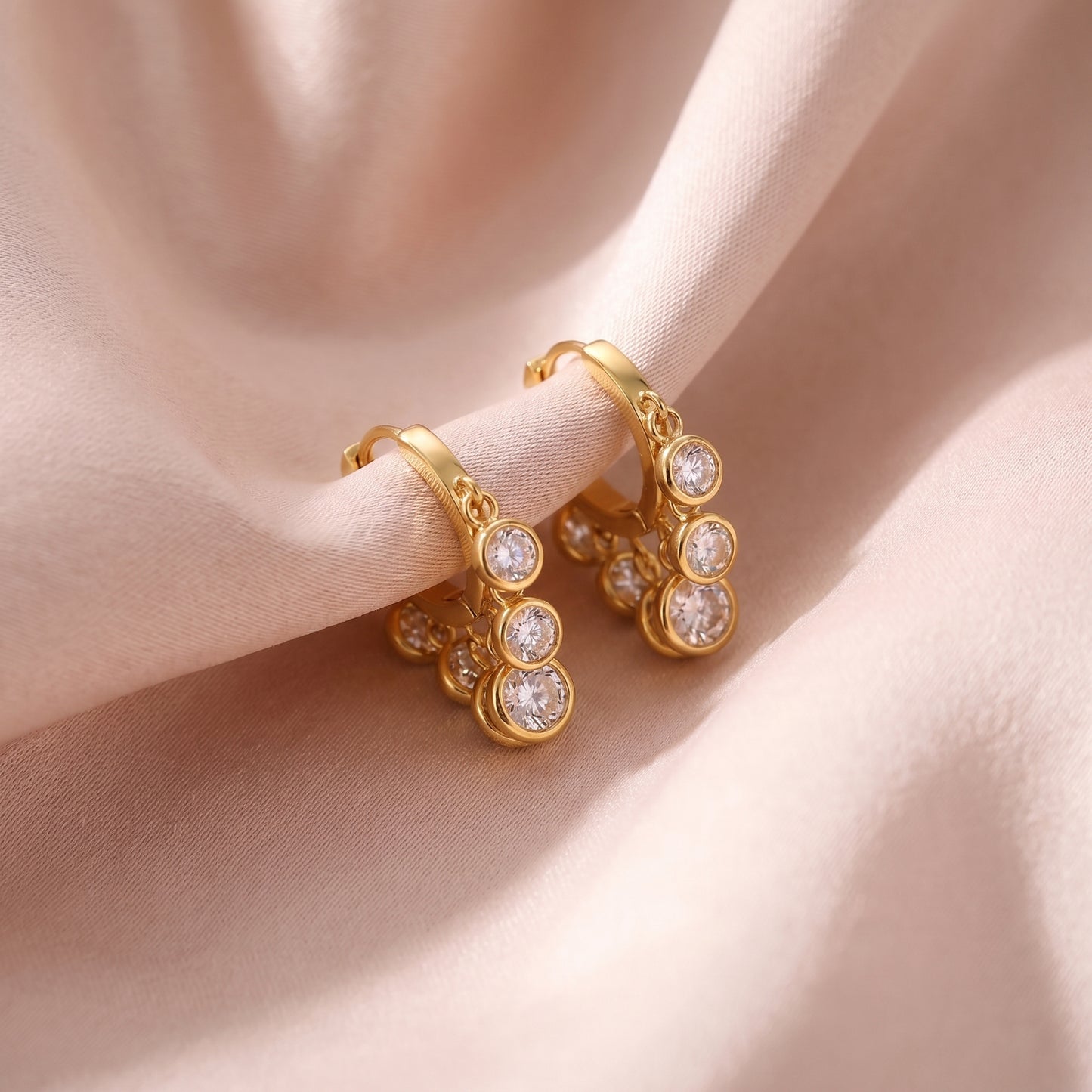 Aesthetic close-up of clear crystal dangle earrings resting on soft pink silk fabric.