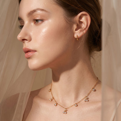 Close-up of a woman wearing Elegant dainty gold necklace featuring alternating bezel-set crystals and micro-pave cherry charms against a neutral background.