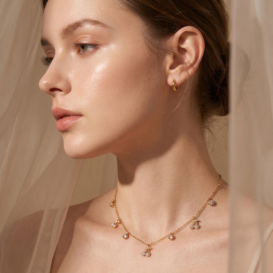 Close-up of a woman wearing Elegant dainty gold necklace featuring alternating bezel-set crystals and micro-pave cherry charms against a neutral background.