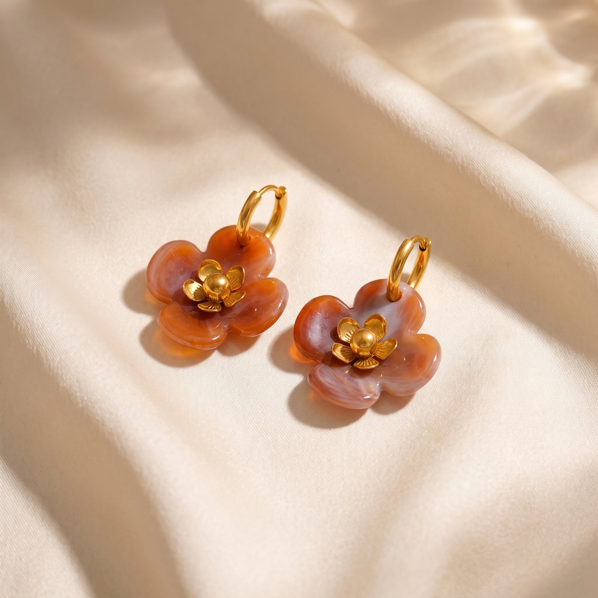 The tarnish-free Fleur Resin Drop Hoops in Warm Amber by Floravisha, displaying marbled orange resin petals and warm gold detailing on a clean white background.