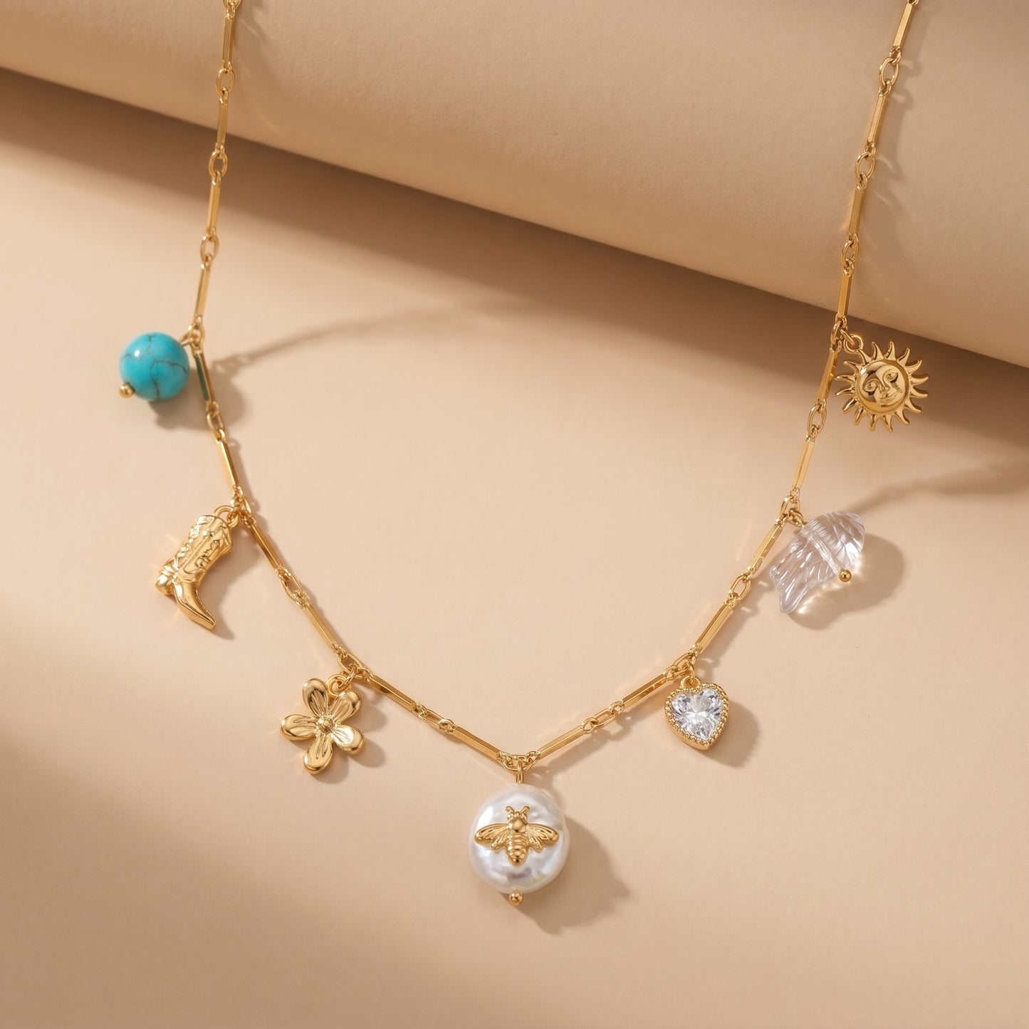 High quality waterproof gold plated charm necklace featuring eclectic pendants including a sun, cowboy boot, bee on a pearl, and a crystal heart, laid flat.