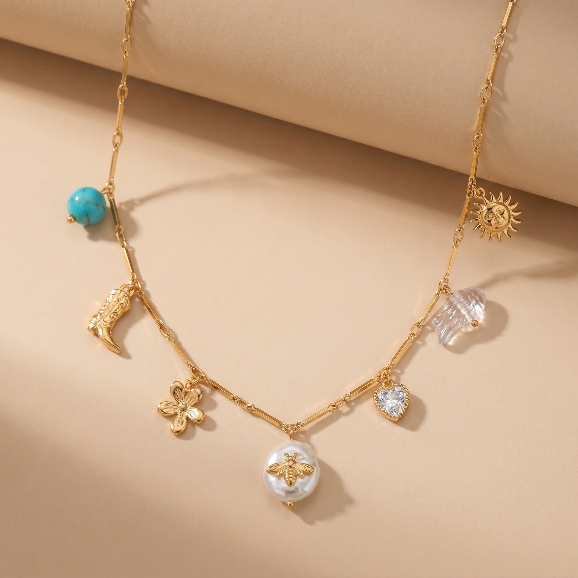 High quality waterproof gold plated charm necklace featuring eclectic pendants including a sun, cowboy boot, bee on a pearl, and a crystal heart, laid flat.