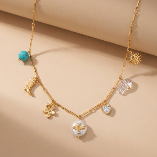 High quality waterproof gold plated charm necklace featuring eclectic pendants including a sun, cowboy boot, bee on a pearl, and a crystal heart, laid flat.