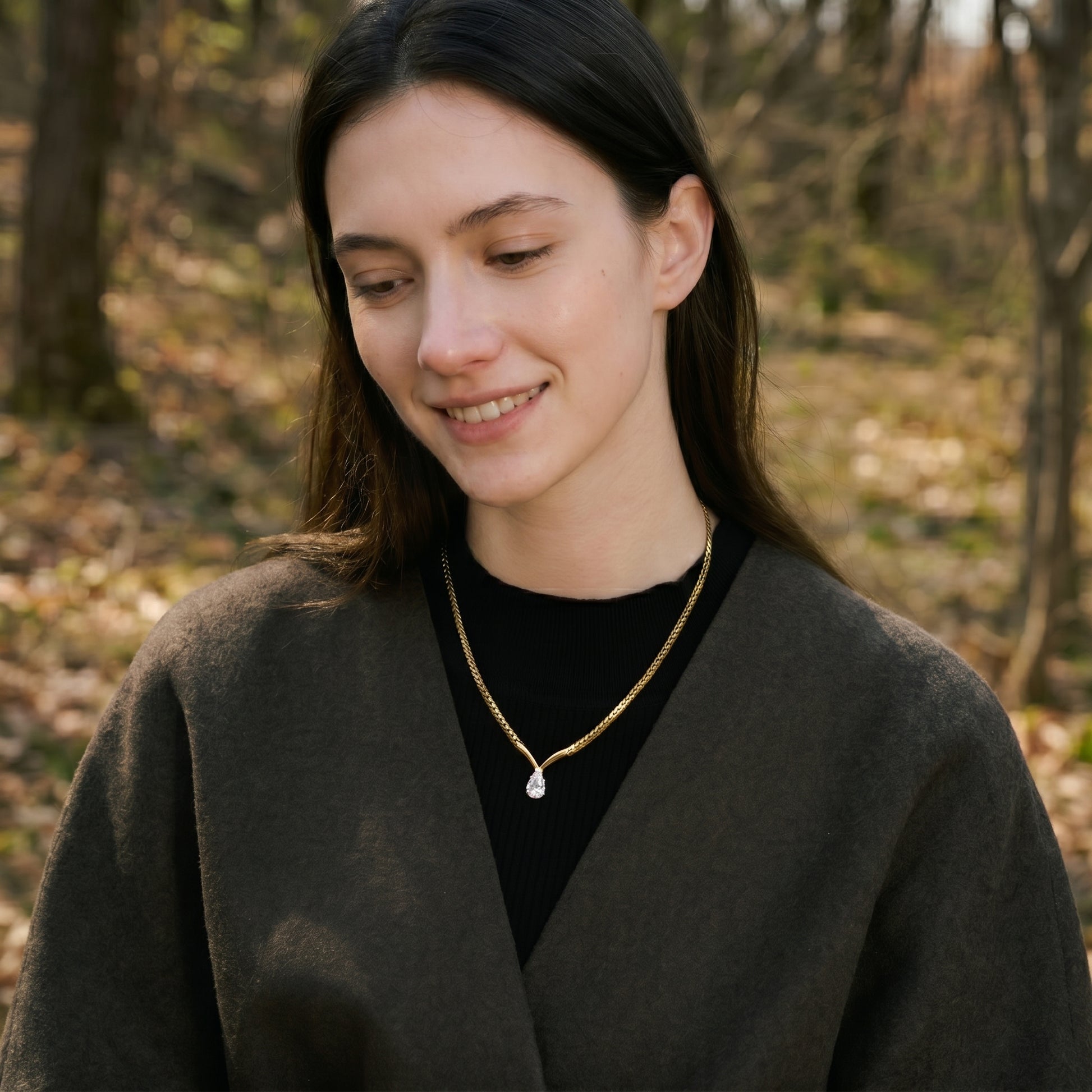 Woman wearing a dark coat and black shirt with a gold necklace in an outdoor setting.