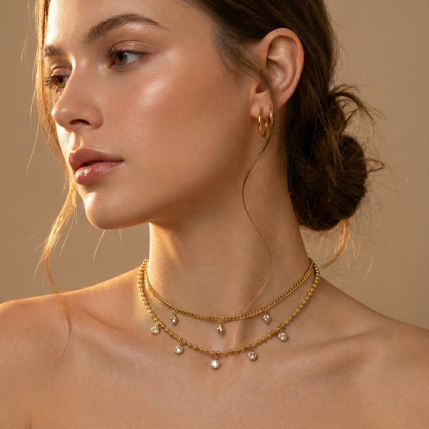 Woman wearing a Elegant, daintier gold-beaded satellite chain necklace featuring alternating dangling bezel-set clear crystals on a clean white background, highlighting its tarnish-free and skin friendly finish against a beige background.