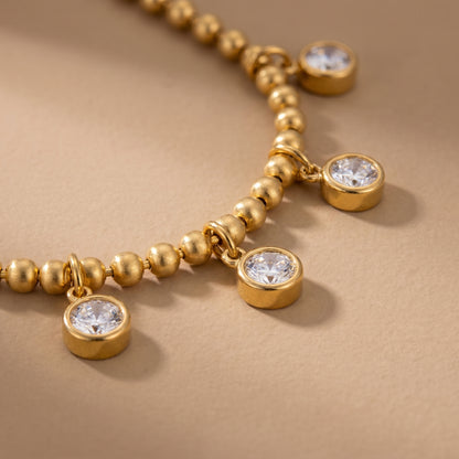 Elegant, daintier gold-beaded satellite chain necklace featuring alternating dangling bezel-set clear crystals on a clean background, highlighting its tarnish-free and skin friendly finish on a beige background.