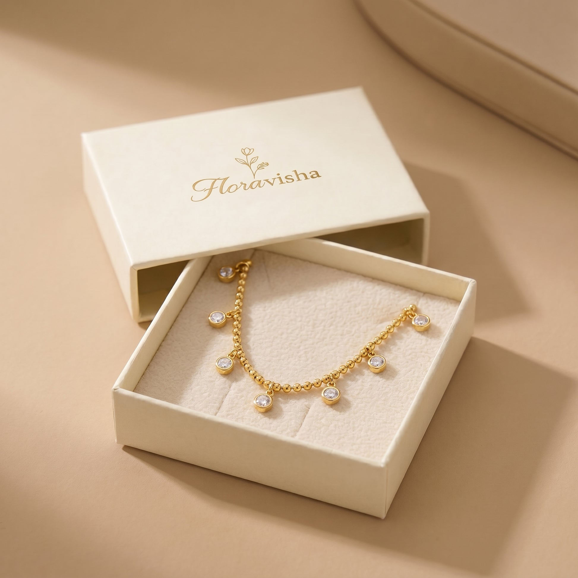 Elegant, daintier gold-beaded satellite chain necklace featuring alternating dangling bezel-set clear crystals, highlighting its tarnish-free and skin friendly finish in an open jewelry box with 'Floravisha' branding on a beige background.