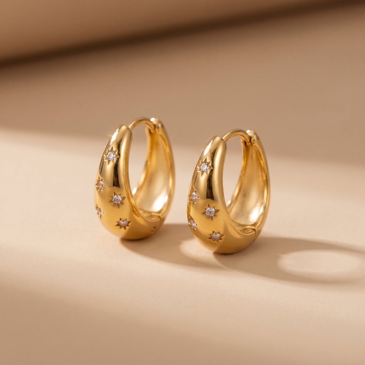 High quality waterproof gold plated chunky dome hoop earrings with engraved starburst crystals, shown standing with a soft reflection on a clean background.
