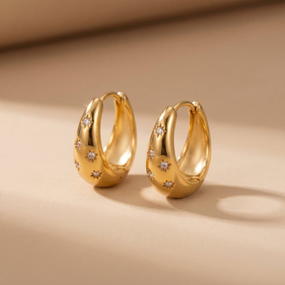 High quality waterproof gold plated chunky dome hoop earrings with engraved starburst crystals, shown standing with a soft reflection on a clean background.