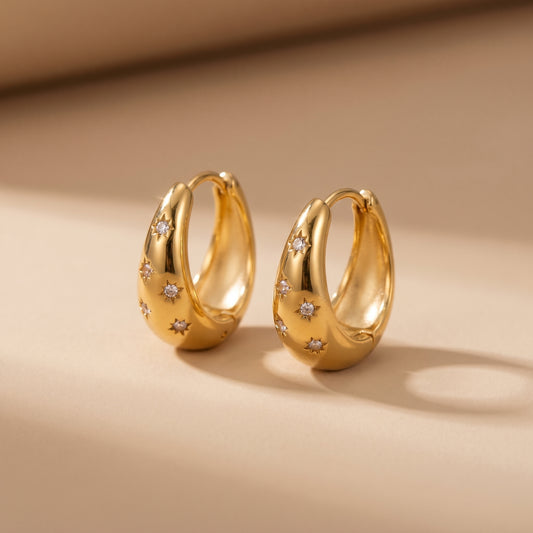High quality waterproof gold plated chunky dome hoop earrings with engraved starburst crystals, shown standing with a soft reflection on a clean background.