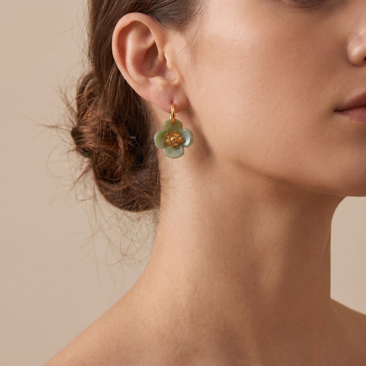 A close-up of a woman's ear wearing a The high quality Fleur Resin Drop Hoops in Sage Green by Floravisha, featuring marbled green resin and gold-plated flower centers on a clean background.