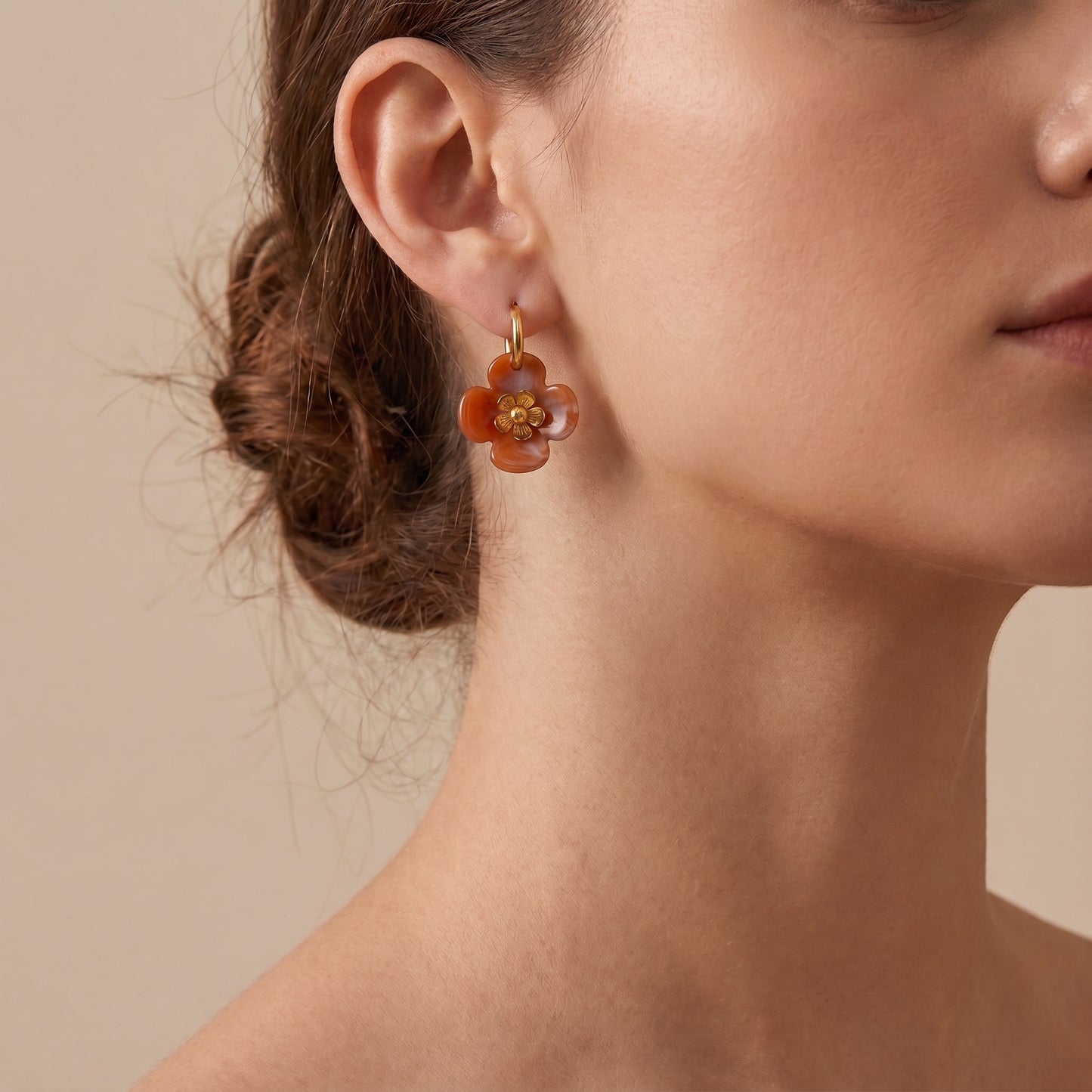 A close-up of a woman's ear wearing a The high quality Fleur Resin Drop Hoops in Warm Amber by Floravisha, featuring marbled green resin and gold-plated flower centers on a clean background.