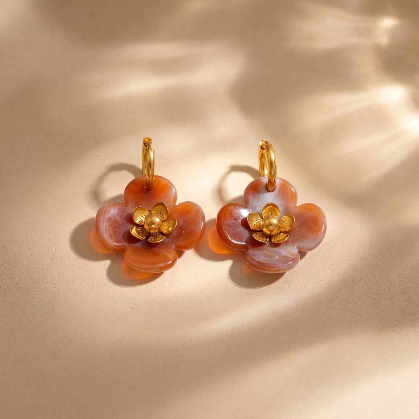 The tarnish-free Fleur Resin Drop Hoops in Warm Amber by Floravisha, displaying marbled orange resin petals and warm gold detailing on a clean background.